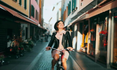 Donna in bici su un viale di negozi Fano e pesaro citta delle biciclette